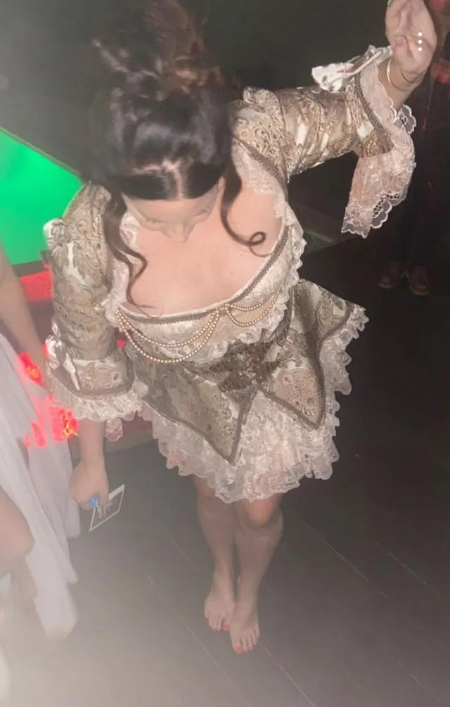 Lana Del Rey standing barefoot indoors in a patterned dress.