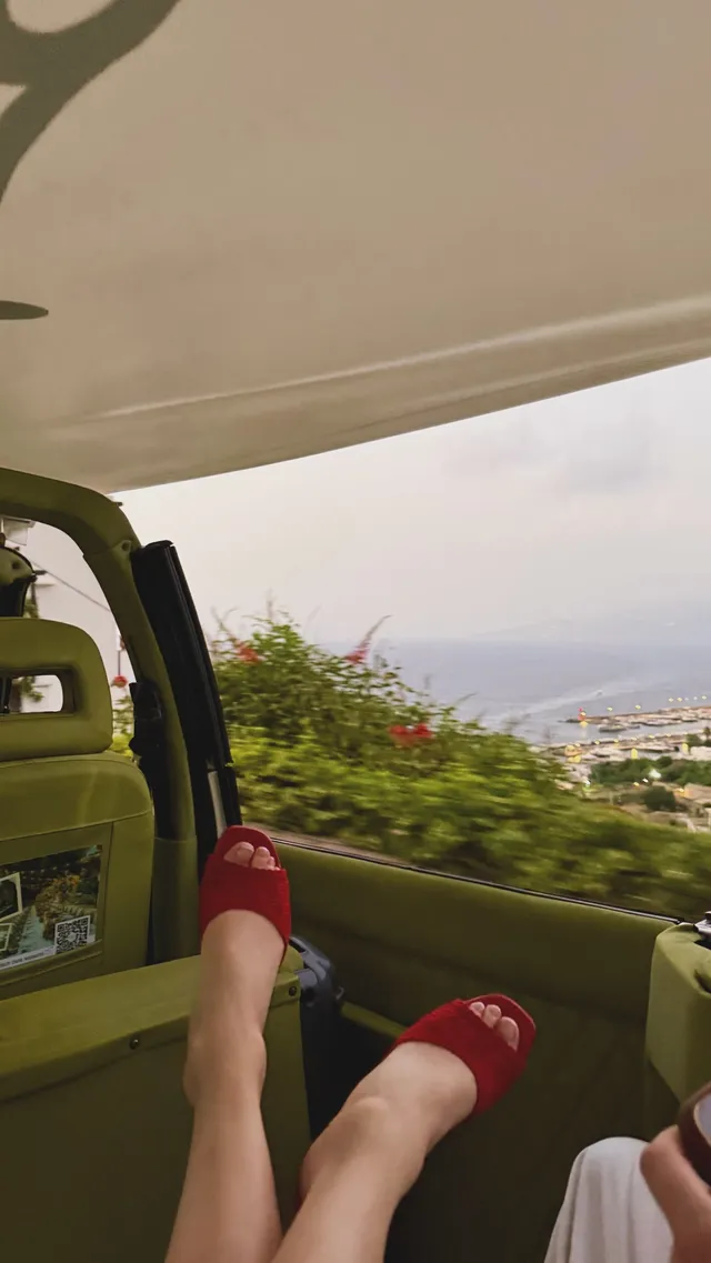 Phoebe Dynevor wearing red sandals while riding in a car.