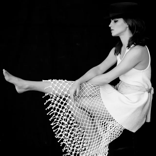 Emma Watson: seated barefoot in a fringed skirt and hat.
