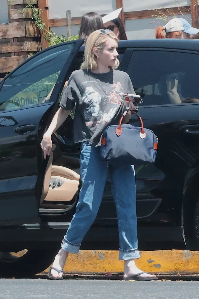 Emma Roberts stepping from a car in jeans and black heeled sandals.