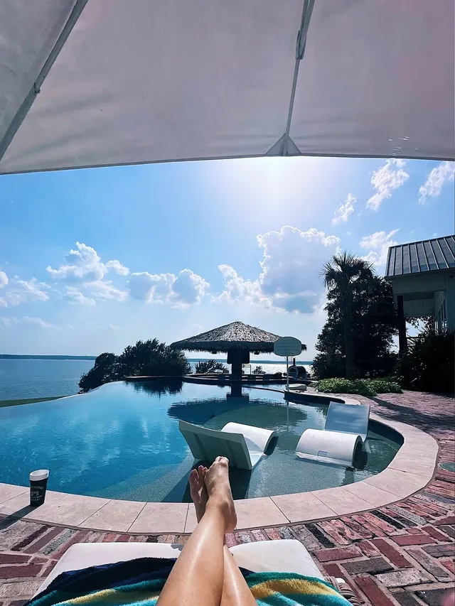 Gwen Stefani resting bare legs on a lounger beside an infinity pool.