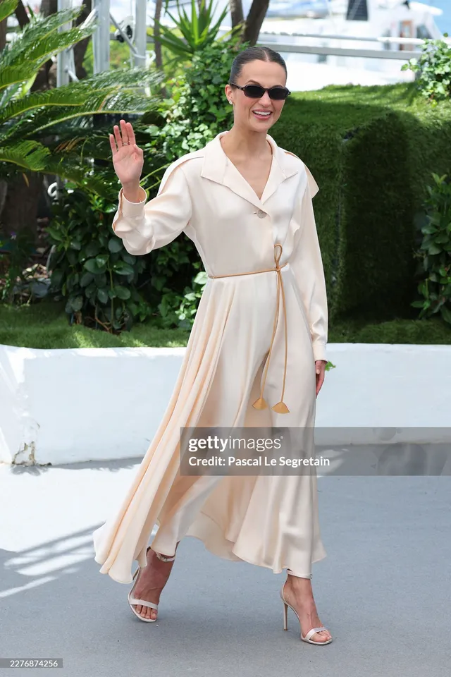 Alicia Vikander walking along a terrace in a cream outfit.