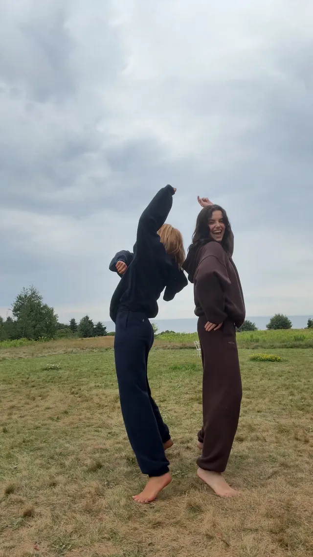Sophie Nélisse jumping barefoot on grass beside another woman.