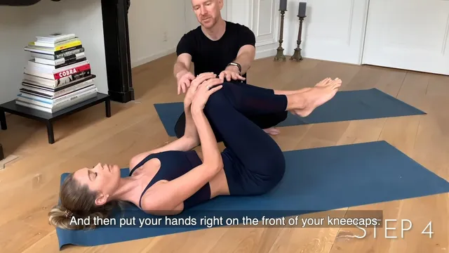 Doutzen Kroes stretching barefoot on a mat with help from an instructor.