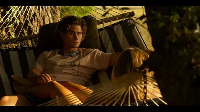 Madelyn Cline reclining barefoot beside a man in a hammock in a film scene.