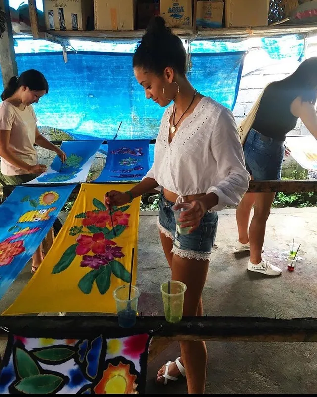 Samantha Logan painting at a table in a white blouse and denim shorts.