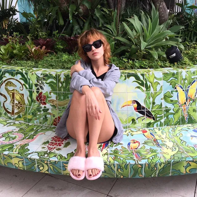 Úrsula Corberó sitting on a patterned outdoor sofa in pink slides.