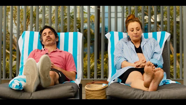 Kaley Cuoco reclining in a striped chair with her bare soles facing forward.