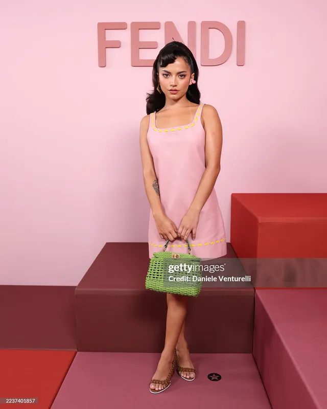 Isabela Merced posing in a pink dress and pale heeled sandals.