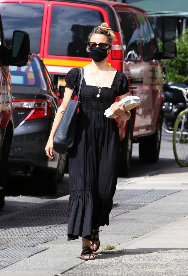 Dianna Agron walking along a city pavement in a black dress.