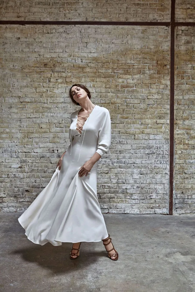Monica Bellucci posing in a white dress against a brick wall.