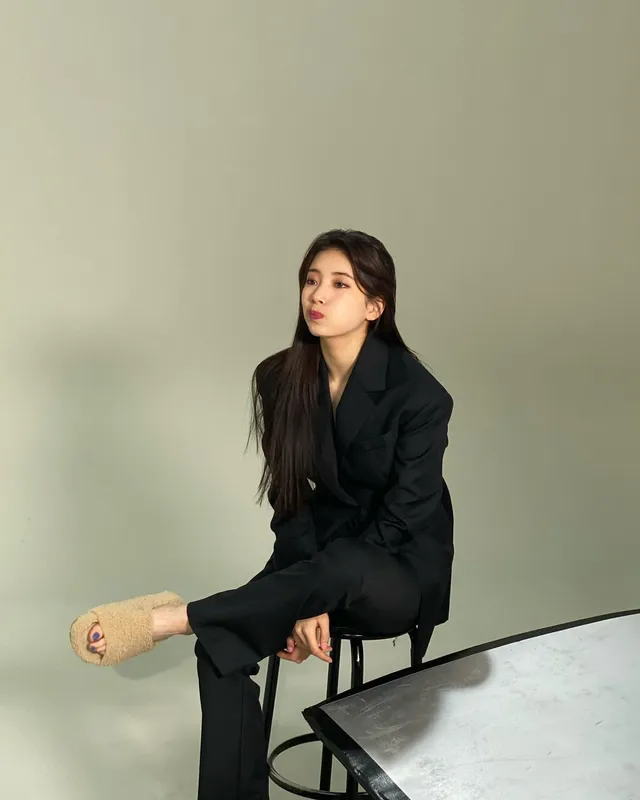 Bae Suzy sitting in a black suit with one shoe removed.
