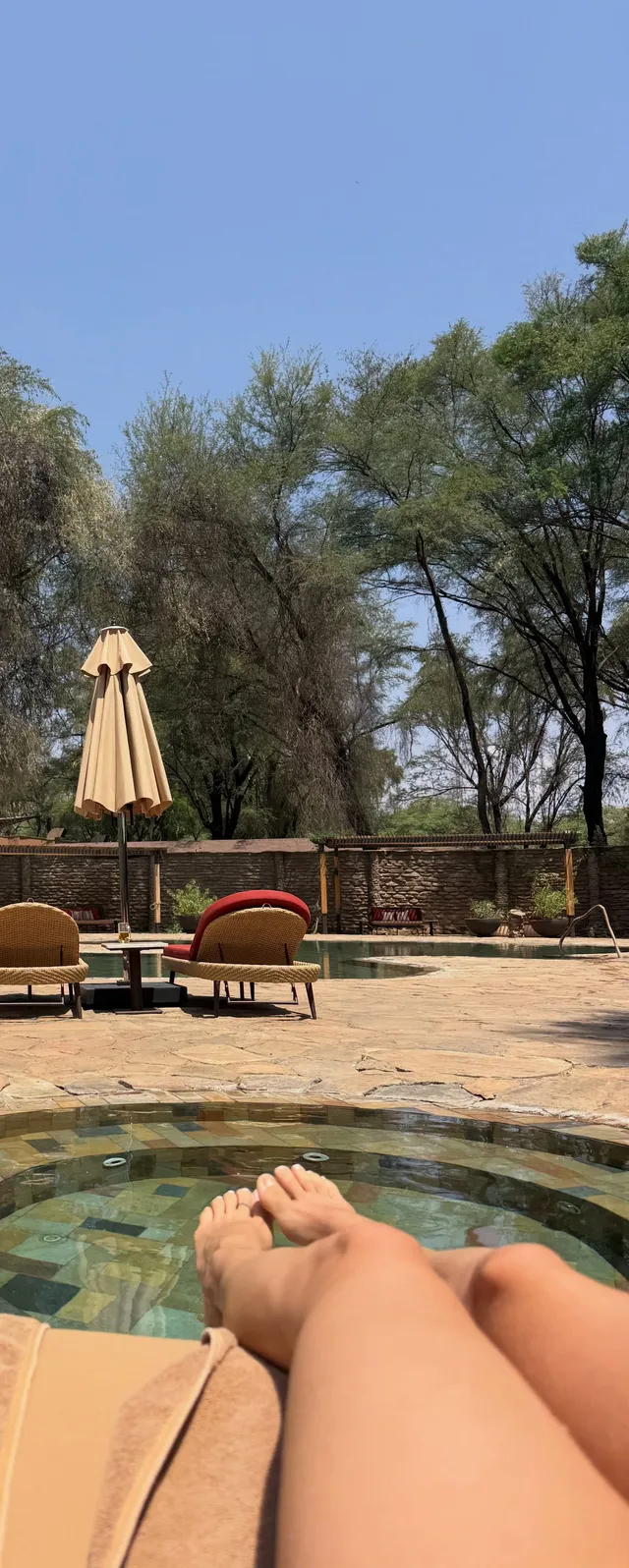 María Pedraza reclining barefoot outdoors near a swimming pool.