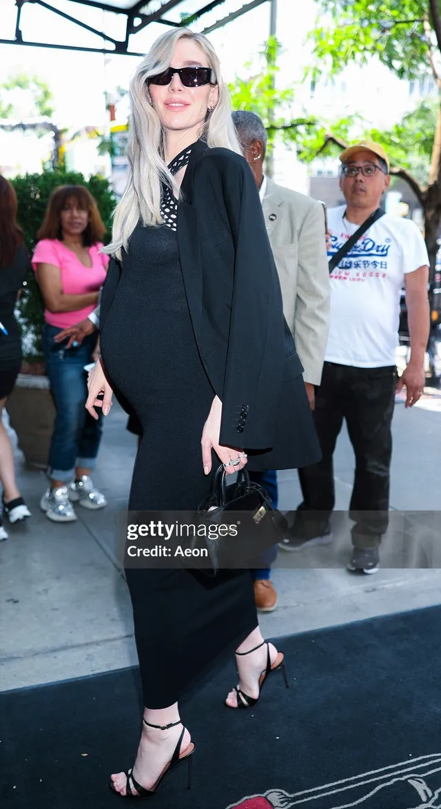 Vanessa Kirby walking outdoors in a black dress and heels.