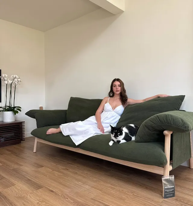 Adelaide Kane relaxing on a green sofa beside a cat.
