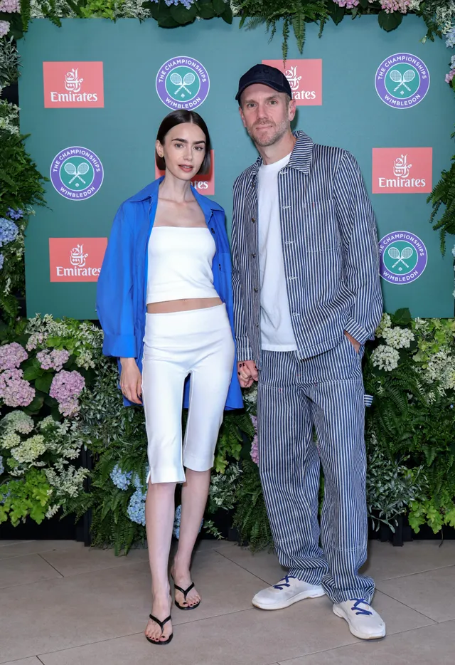 Lily Collins standing beside a man in a blue blazer and flat sandals.