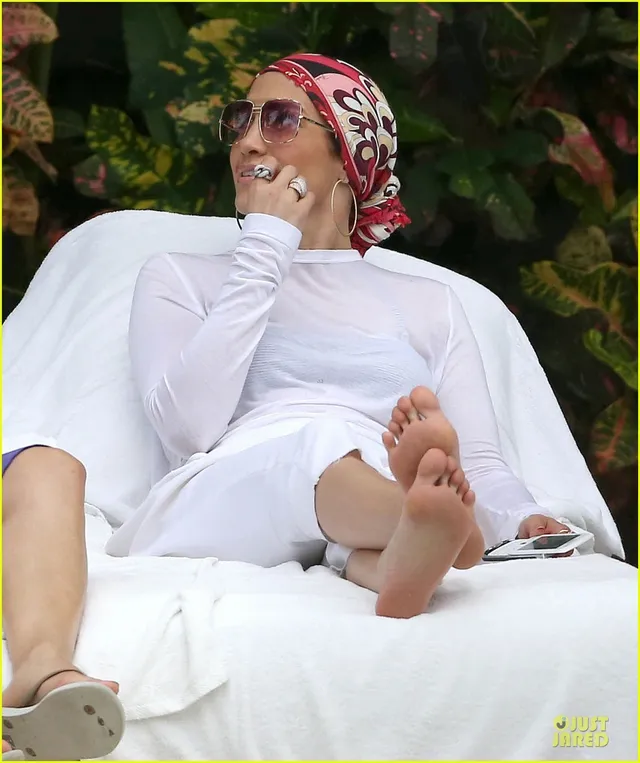 Jennifer Lopez a relaxed white outfit with one foot raised.