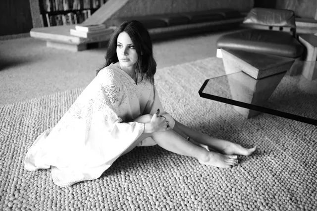 Lana Del Rey sitting barefoot on a carpet in a monochrome portrait.