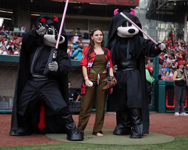 Dafne Keen posing barefoot on a baseball field with mascots.