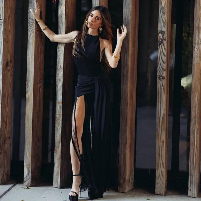 Sarah Shahi posing beside a doorway in a long black dress.