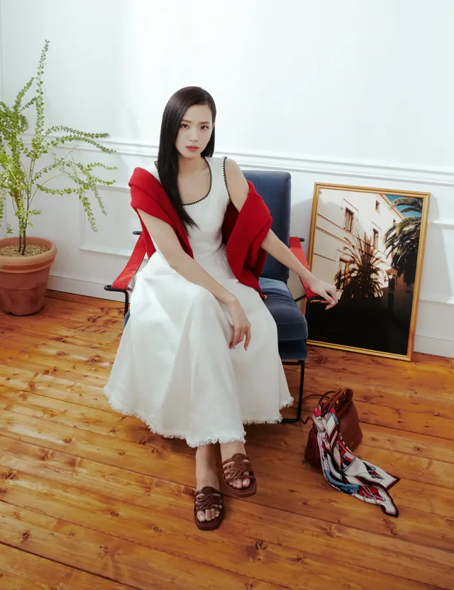 Jisoo sitting in heeled sandals and a white dress with a red jacket during a fashion shoot.