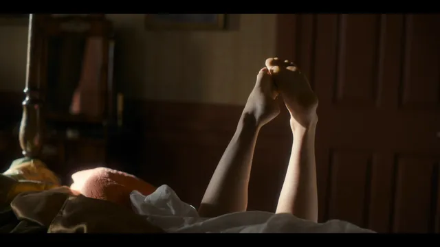Alice Eve reclining on a bed with her legs raised in a scene.