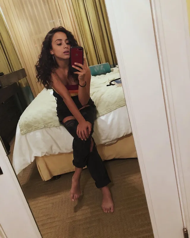 Kiana Madeira taking a mirror selfie barefoot in a dark outfit.