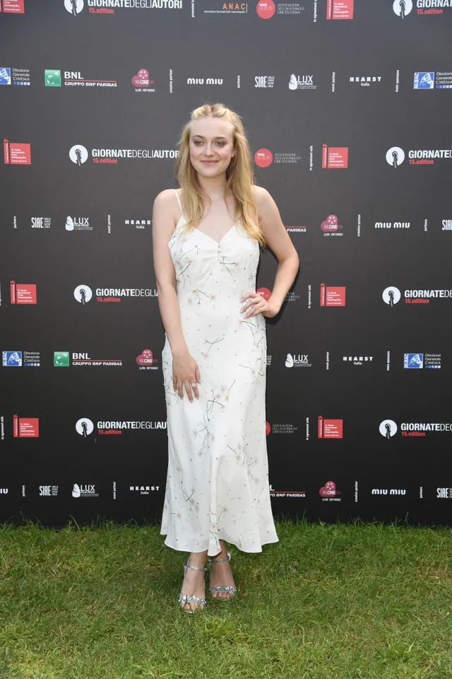 Dakota Fanning posing in a white dress and silver heels on a lawn.