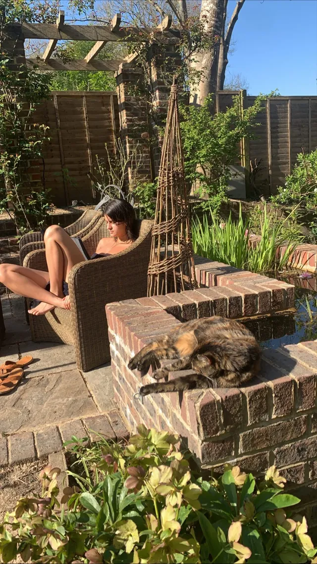 Anya Chalotra relaxing barefoot in an outdoor chair near a garden.