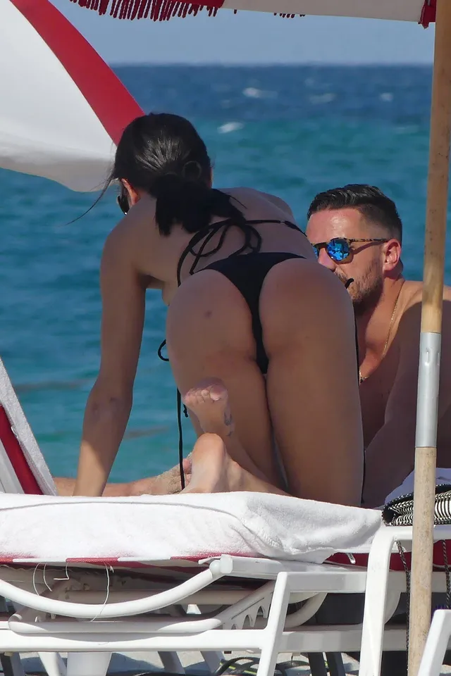 Adriana Lima sitting barefoot on a beach lounger.