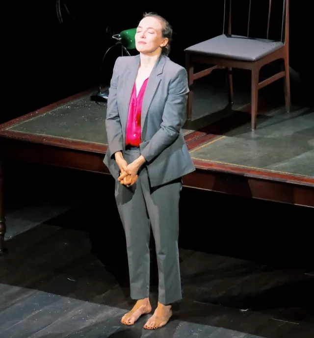 Jodie Comer standing onstage in a grey suit and pink blouse.