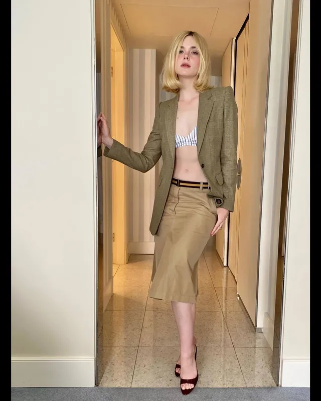 Elle Fanning posing indoors in a khaki skirt, blazer and heeled sandals.
