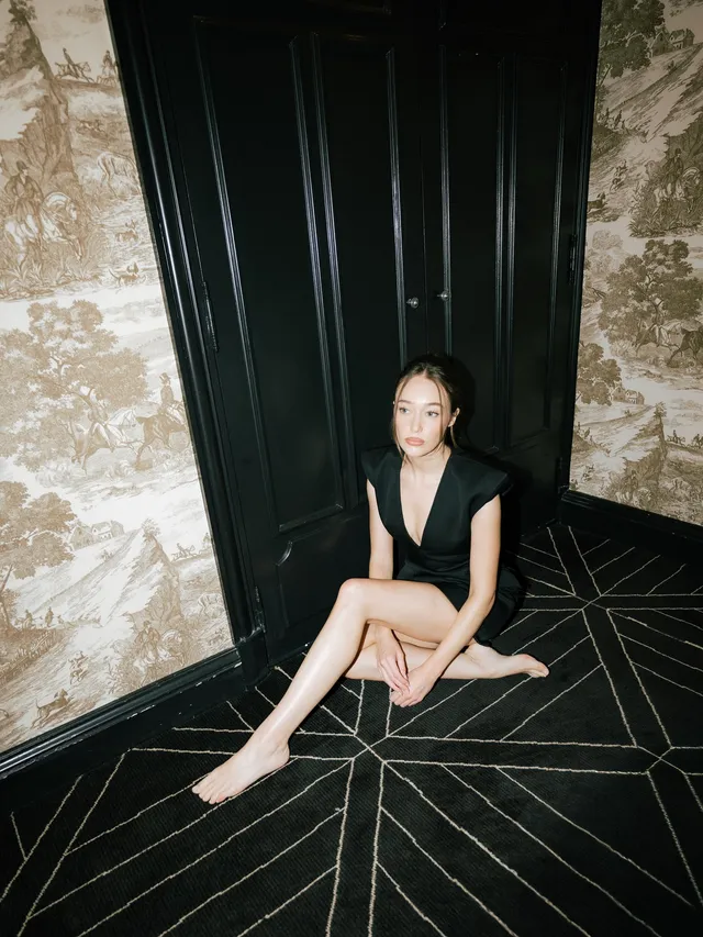 Alycia Debnam-Carey sitting on a patterned floor in a black dress.