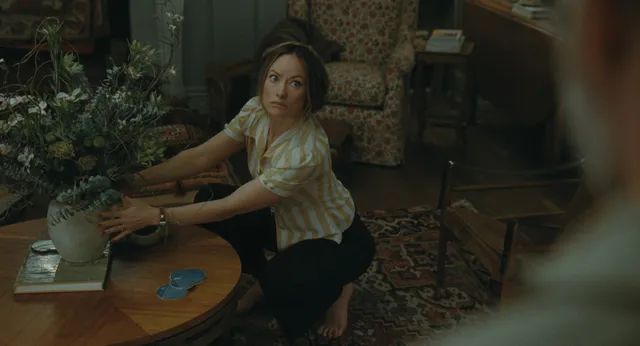Olivia Wilde sitting cross-legged on a sofa with bare feet visible in a film scene.