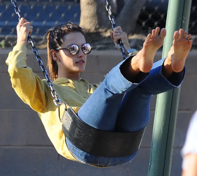 Alessandra Ambrosio sitting on a swing with bare soles facing the camera.