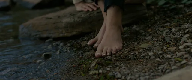 Anna Kendrick showing a bare foot beside a woodland stream.