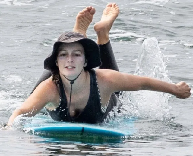 Leighton Meester paddling on a surfboard wearing a sun hat.