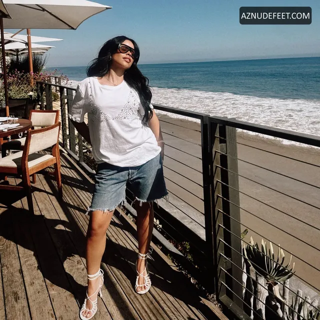 Cierra Ramirez in an oversized white shirt, denim shorts and flip-flops beside the ocean.