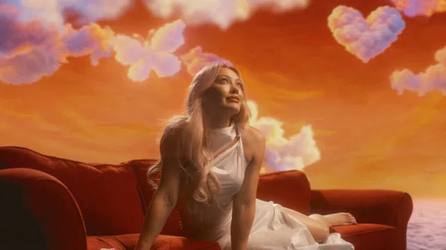 Hilary Duff reclining barefoot on a sofa in a colorful studio scene.