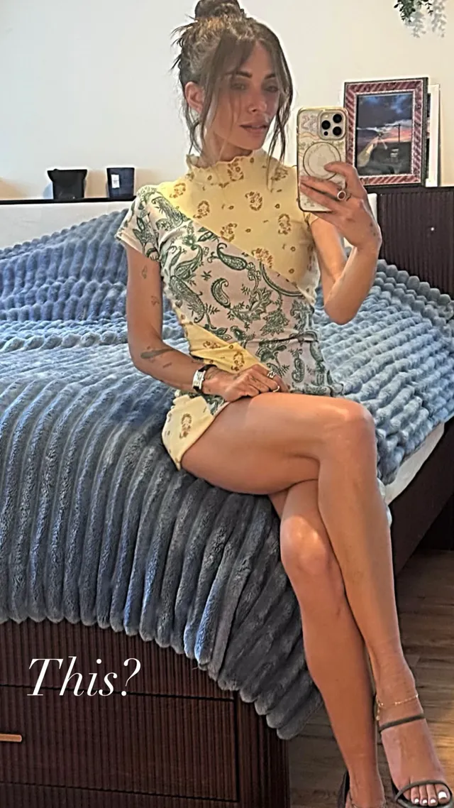 Sarah Shahi taking a seated mirror portrait in a yellow dress.