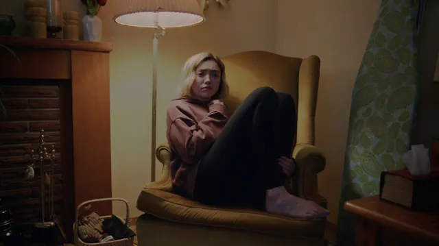 Peyton List sitting barefoot in an armchair in a screen scene.