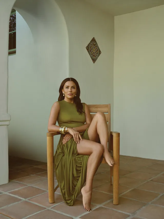 Eva Longoria sitting on a wooden chair in a green dress.
