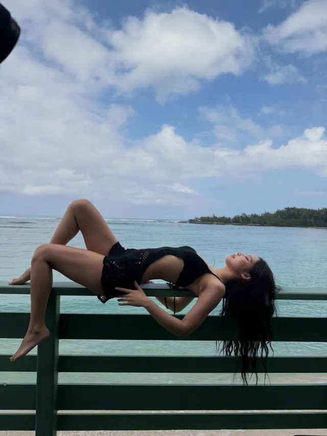 Jennie Kim reclining barefoot on a boat railing beside the sea.