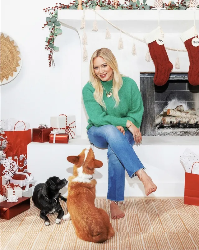 Hilary Duff sitting beside two dogs with one bare foot raised.