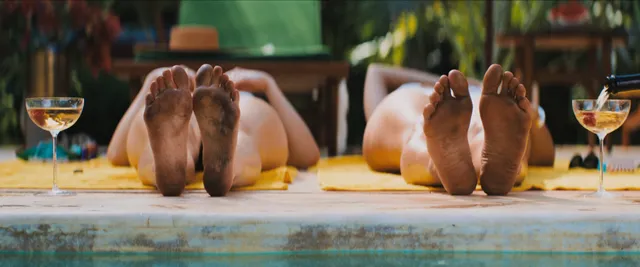 Adria Arjona resting barefoot beside another person at a swimming pool.