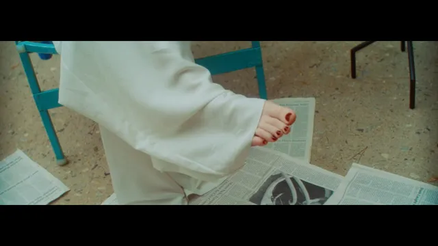 Billie Eilish a screen detail of a bare foot below pale trousers.
