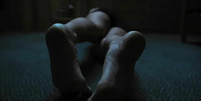 Alice Eve lying on a floor in a dimly lit screen scene.