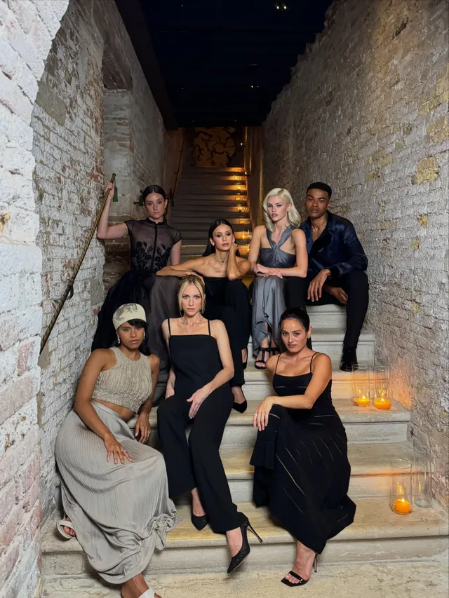 Chase Sui Wonders posing with cast members on stairs in black heels.