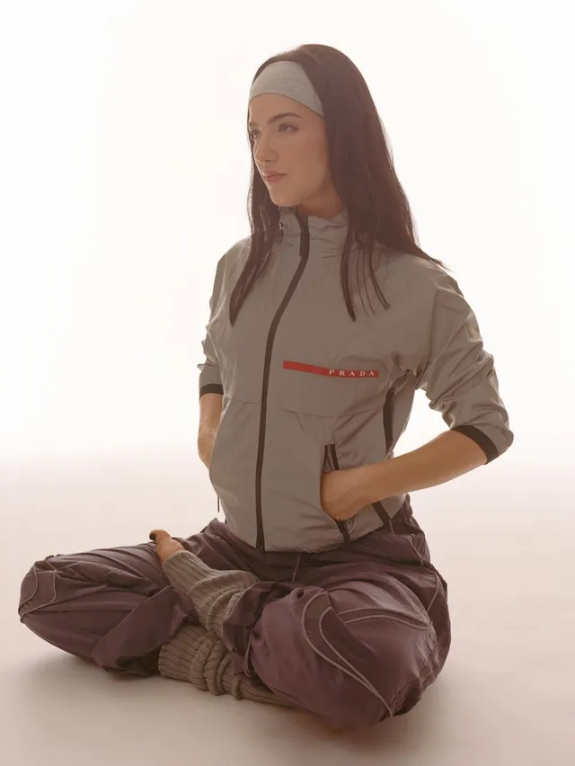 Charli D’Amelio sitting barefoot in an athletic outfit for a studio portrait.