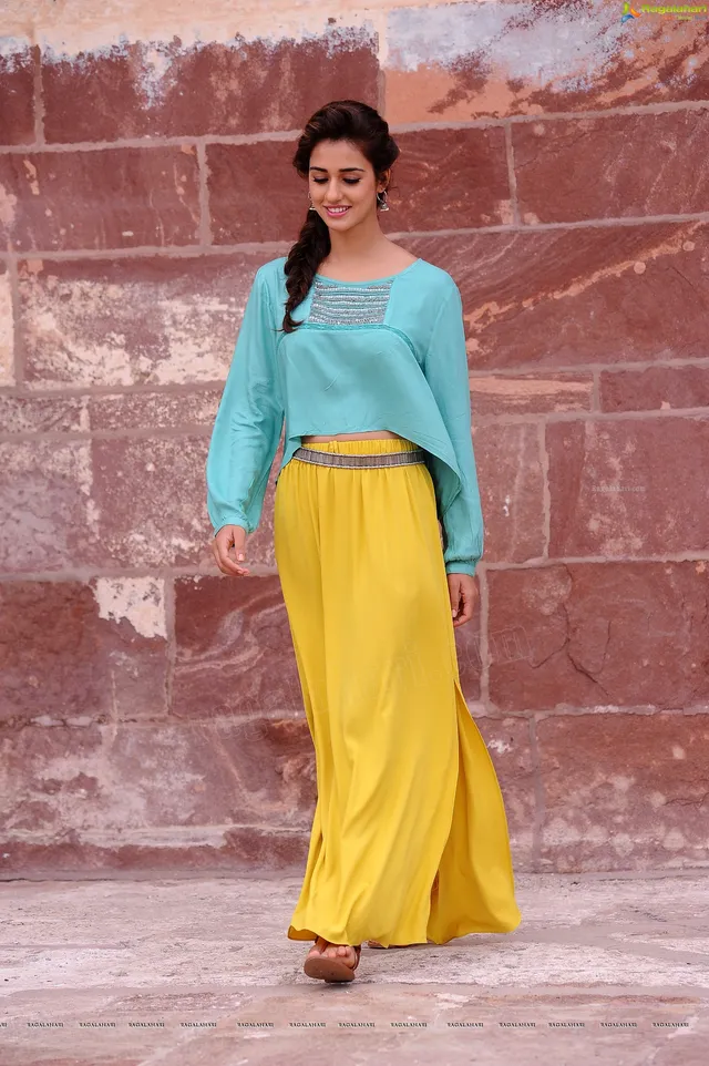 Disha Patani walking in flat sandals beneath flowing yellow trousers.